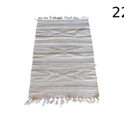 Bohemian or Moroccan style rug in beige or ivory tones, characterised by its linear geometric design and fringes at the ends, for rent for events, advertising, films and series.