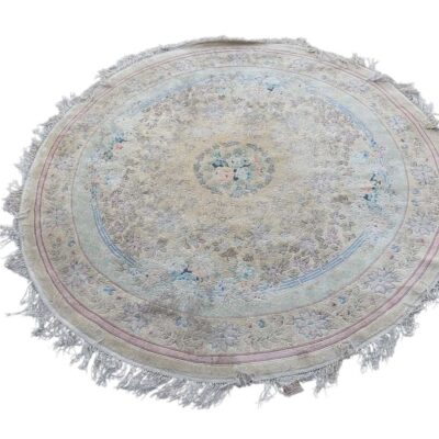Alfombra persa redonda tipo Tabriz en color crudo con patrones florales delicados y acentos en azul y rosa, acabada con un borde de flecos alquiler para eventos, publicidad, peliculas y series