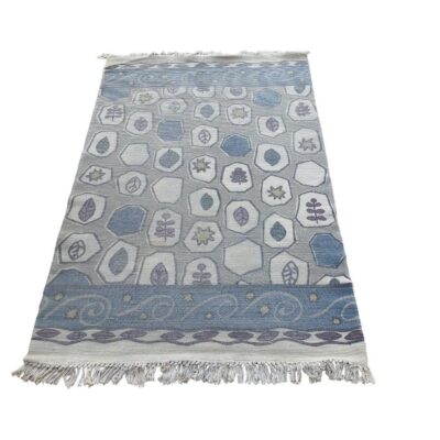 Alfombra tipo kilim tejida a mano con patrones geométricos en tonos azules y grises, y flecos en los extremos alquilr para eventos,publicidad, peliculas y series